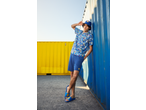 Man in Lidl pixelated shirt, blue shorts, bucket hat, and slides, leaning on a blue container.