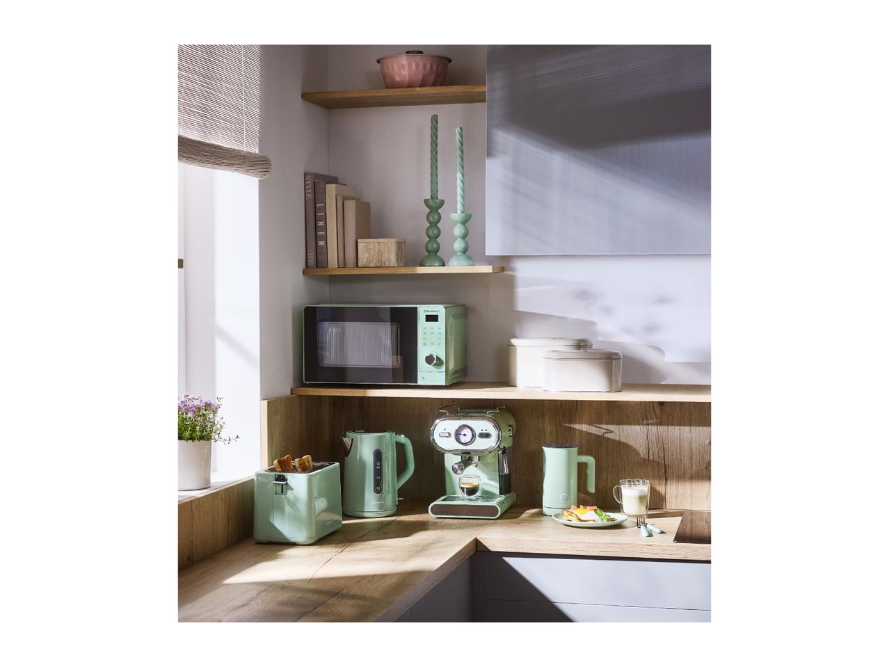 Mint green kitchen appliances: microwave, toaster, kettle, and espresso machine on a wooden counter.