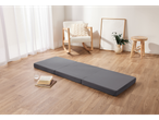 A tri-fold gray floor mattress rests on light wood flooring in a minimalist living room.
