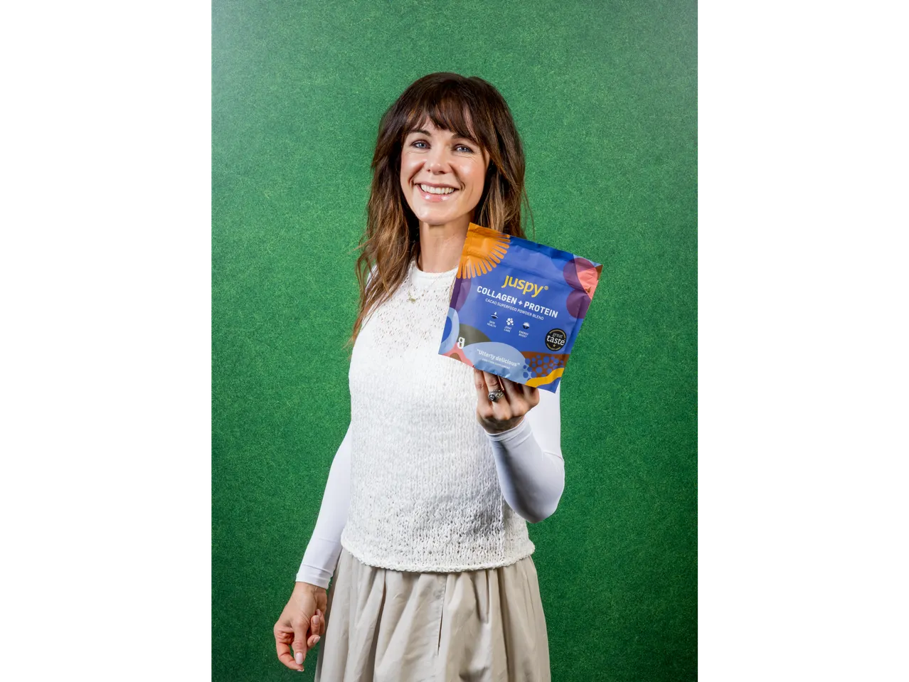 A woman smiling and holding a Juspy Collagen + Protein cacao superfood powder blend.