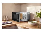 Microwave oven with an open door on a kitchen counter, next to a bowl of soup.