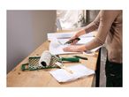 Person cutting wallpaper with a utility knife, with painting tools on a wooden table.