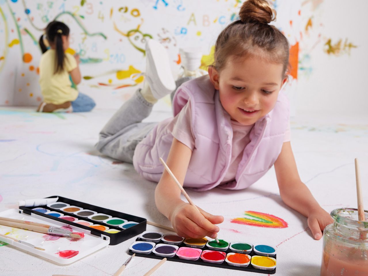 Bambina che dipinge un arcobaleno con acquerelli su un foglio bianco.