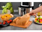 Mão a pegar num forro de papel para fritadeira de ar, ao lado de uma fritadeira, nuggets e vegetais.