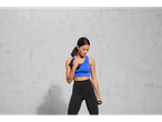 Woman in blue sports bra and black leggings holding two dumbbells.