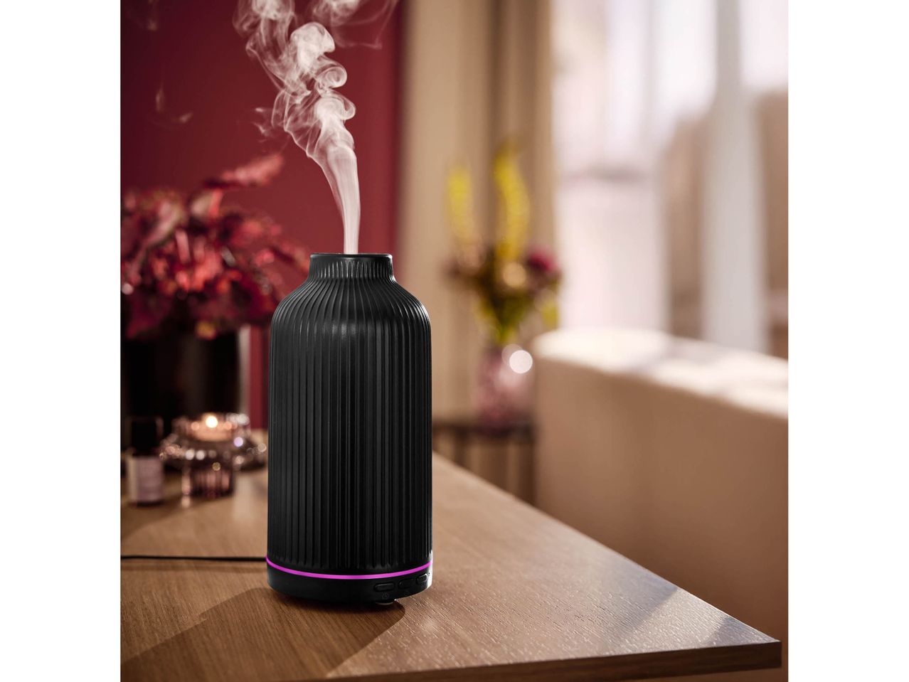 Un diffusore di aromi nero con fumo che fuoriesce, su un tavolo di legno.