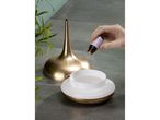 A hand adding essential oil to a gold and white aroma diffuser.
