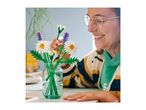 Smiling person arranging a bouquet of toy flowers in a glass vase.