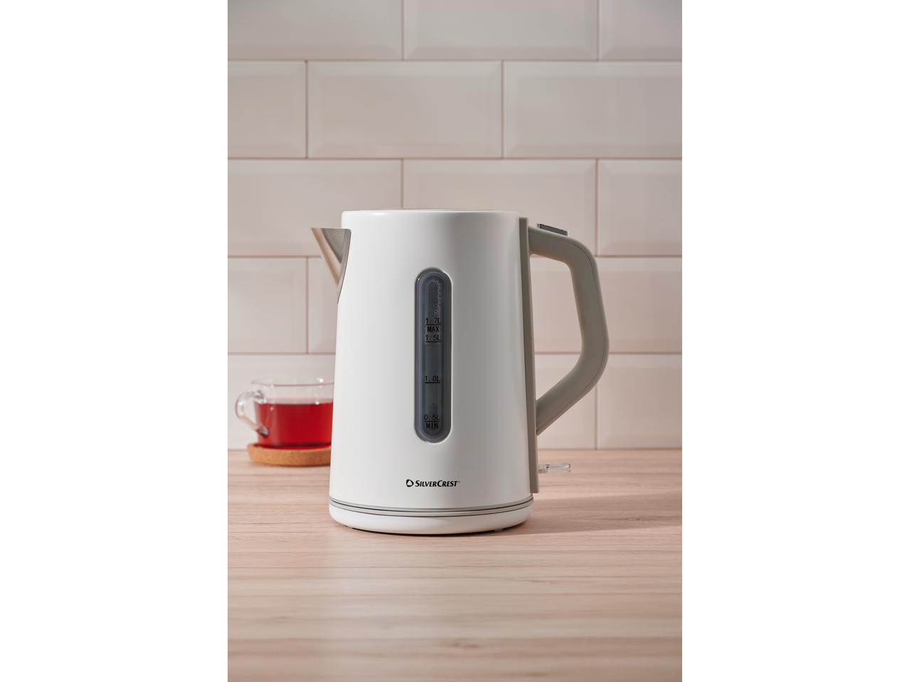 White electric kettle with water level indicator and a cup of tea on a wooden surface.
