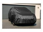 Black car cover on a car parked on a paved driveway in front of a garage.