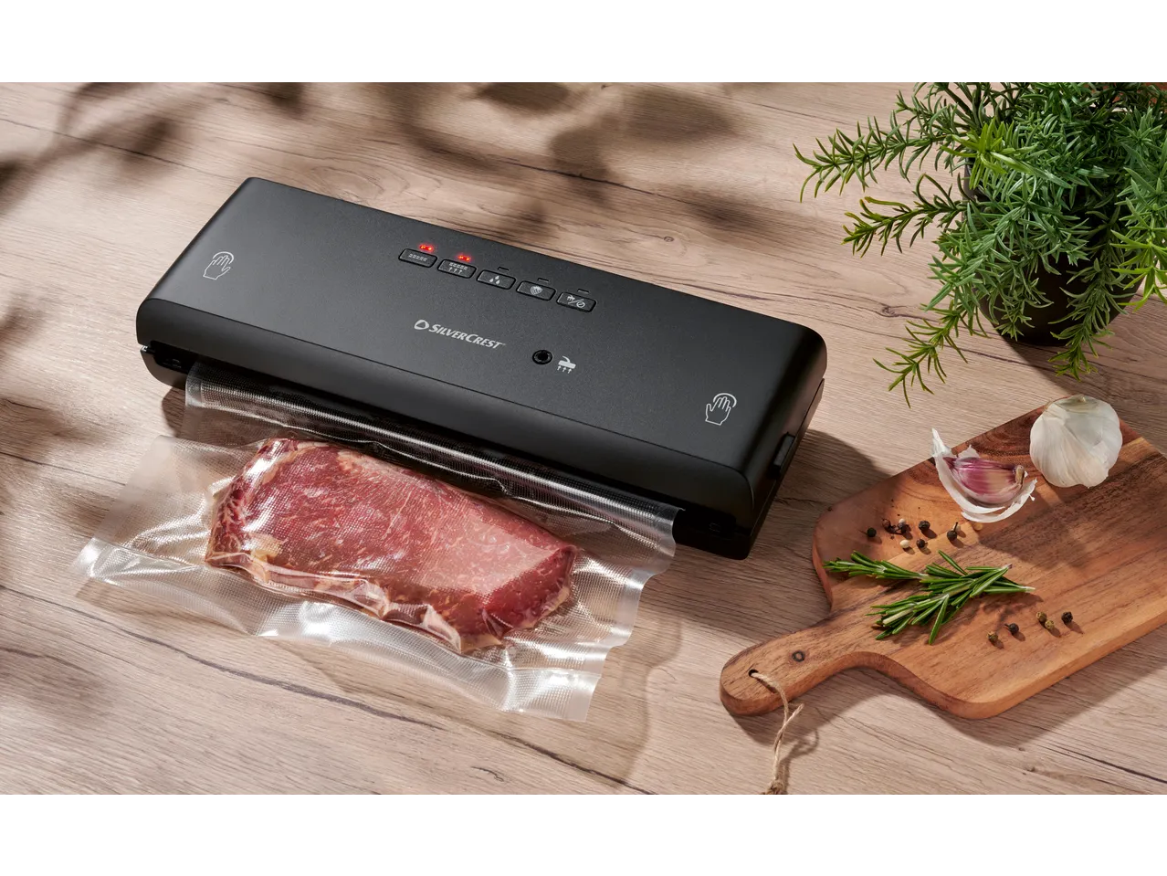 SILVERCREST® Vacuum Sealer with meat in a vacuum bag, garlic, and rosemary on a wooden board.