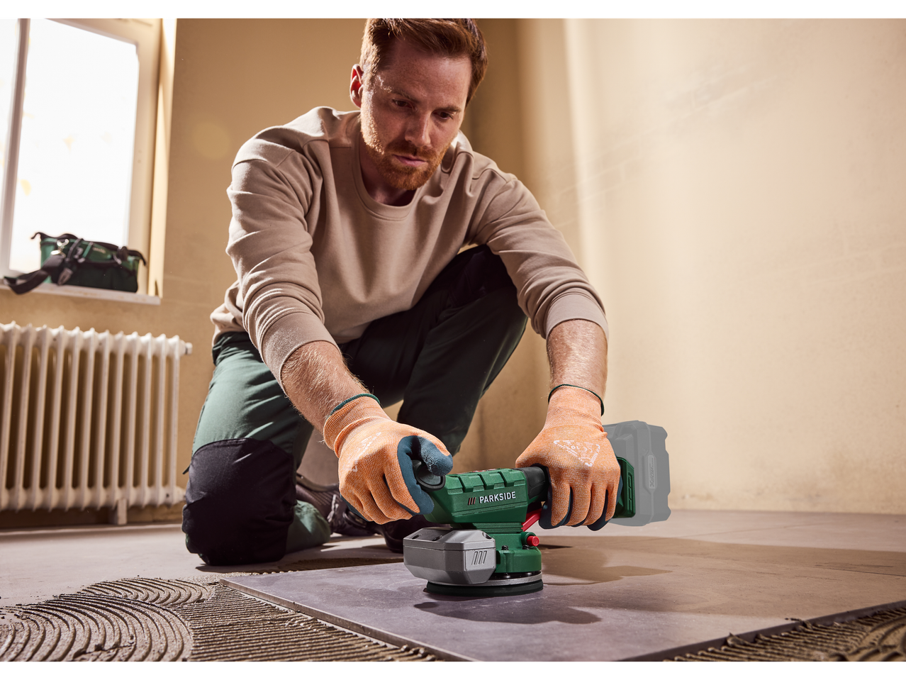 Homem usa vibrador de azulejos PARKSIDE® no chão.