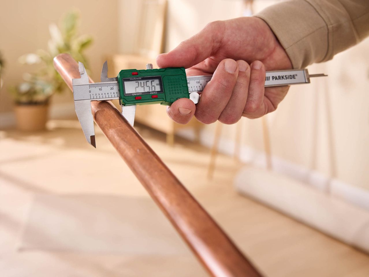 A person using a Parkside digital caliper to measure the diameter of a copper pipe.