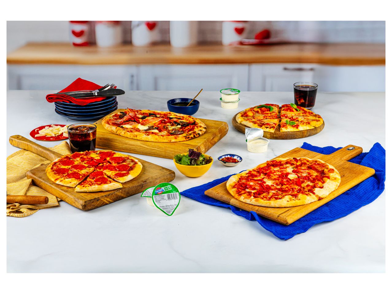 Several small, ready-to-eat pizzas on wooden boards, alongside drinks and toppings.