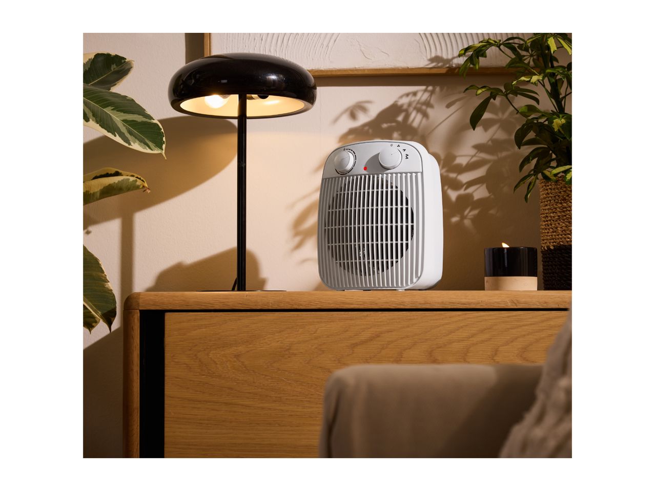White fan heater on a wooden cabinet with a black lamp and plants.