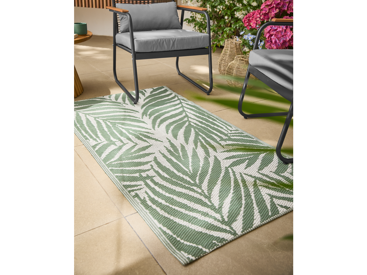 Zeleni spoljni tepih sa dezenom palminog lišća, baštenskim nameštajem i biljkama.