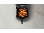 Vedere de sus a unei friteuze cu aer pline cu pulpe de pui crocante pe o suprafață de marmură.
