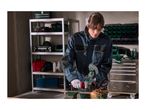 A person using a cordless angle grinder to cut metal in a workshop.