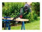 A person using a cordless mini chainsaw to cut a wooden plank outdoors.