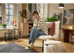 Femeie așezată pe scaun cu spațiu de depozitare, înconjurată de mobilier și decor modern.