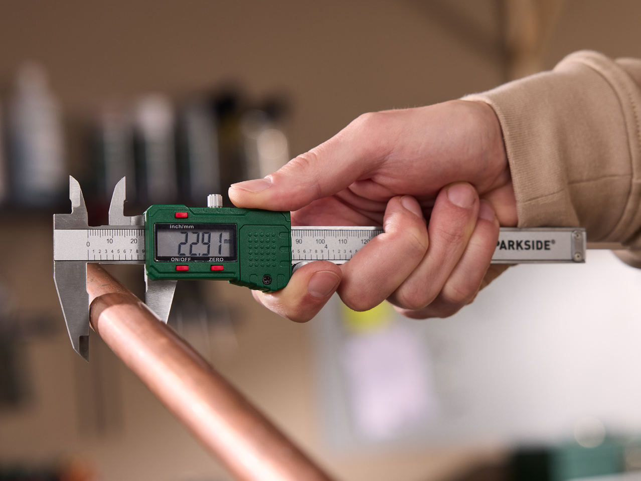 Ръка, държаща цифров шублер, измерващ медна тръба, показващ 22,91 мм.