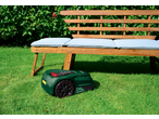 Robotic lawnmower on green grass next to a wooden garden bench with light blue cushions.