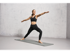 Woman in black leggings and top practicing yoga on a grey mat.