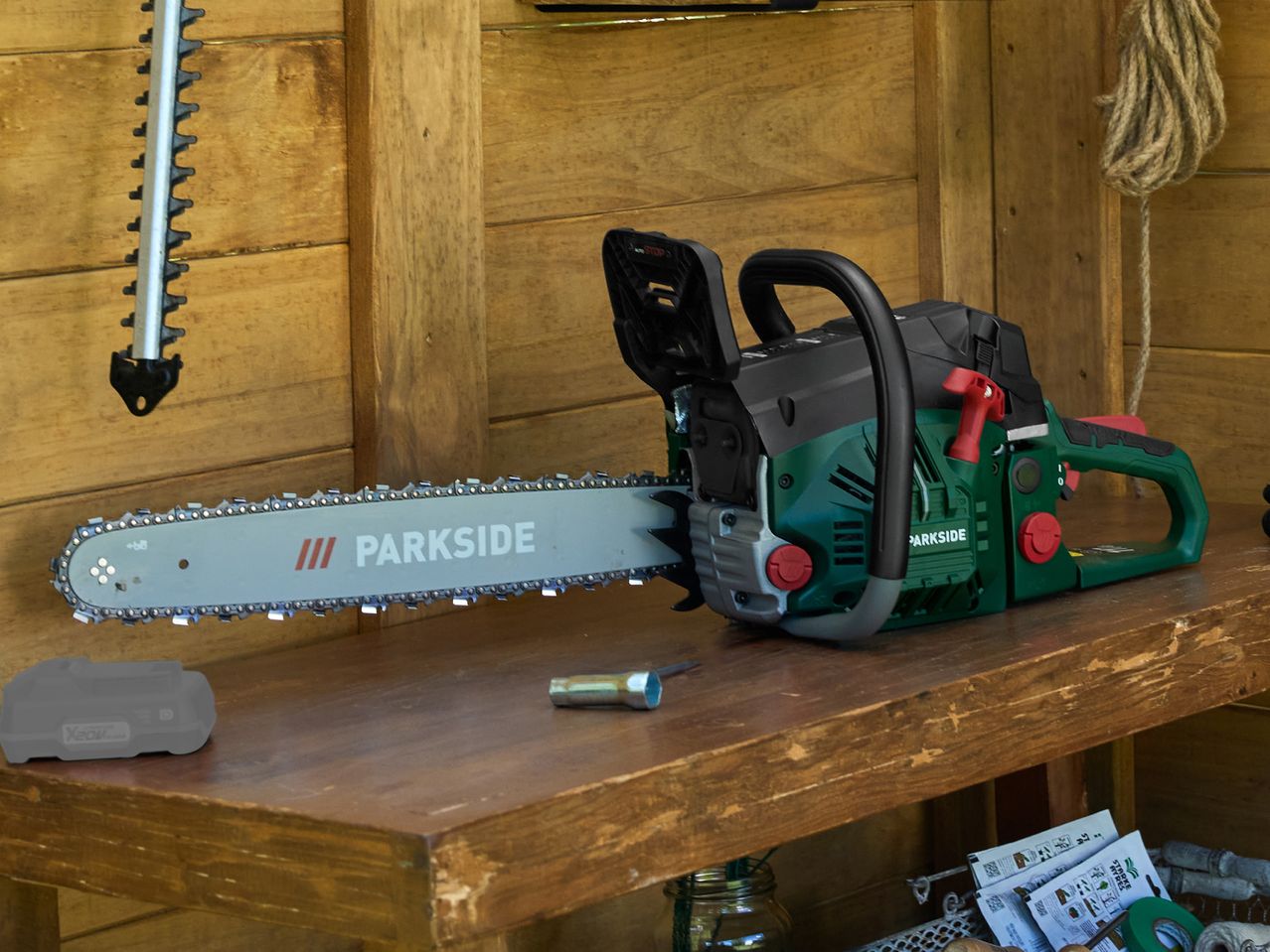 A green and black chainsaw with a long blade on a wooden workbench, next to a battery pack.