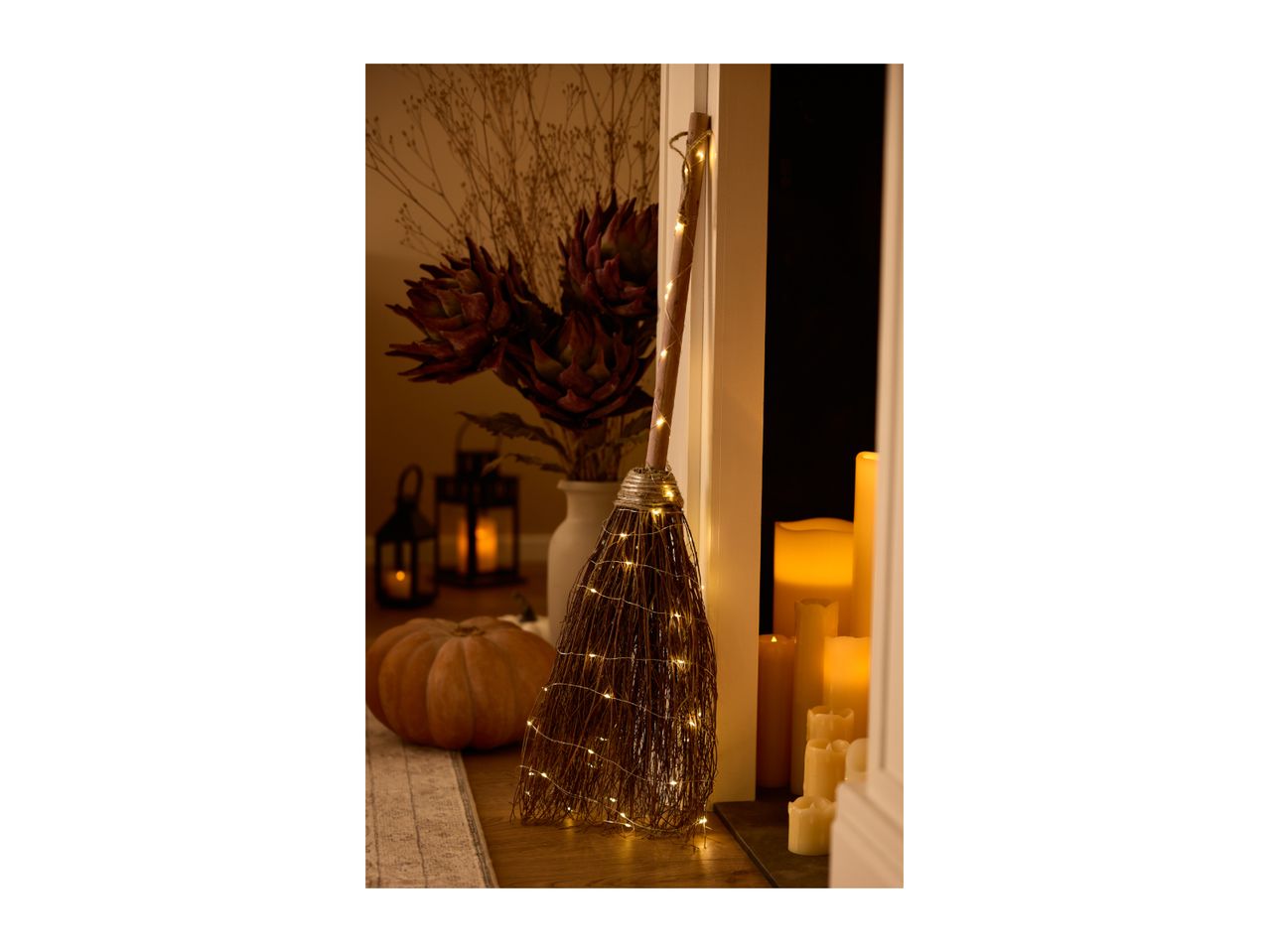 Decorative witch's broom with LED lights next to a pumpkin and candles