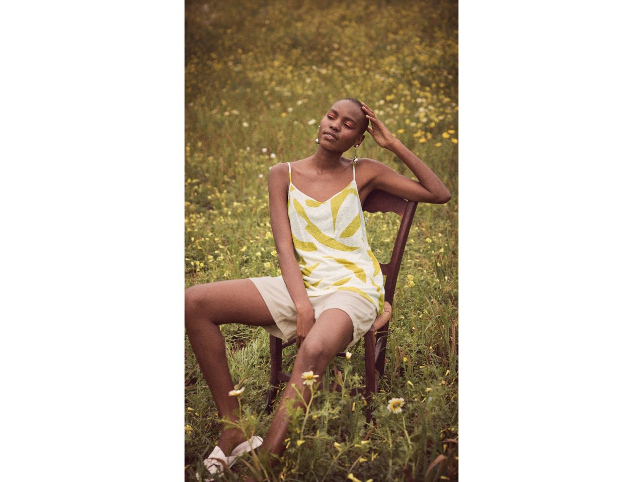 Donna con top giallo e pantaloncini beige seduta su una sedia in un campo fiorito.