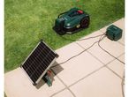 Robotic lawnmower and solar panel charging station on a patio next to grass.