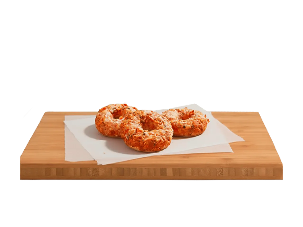 Trois bagels salés au fromage et aux herbes sur du papier sulfurisé, sur une planche à découper en bois.