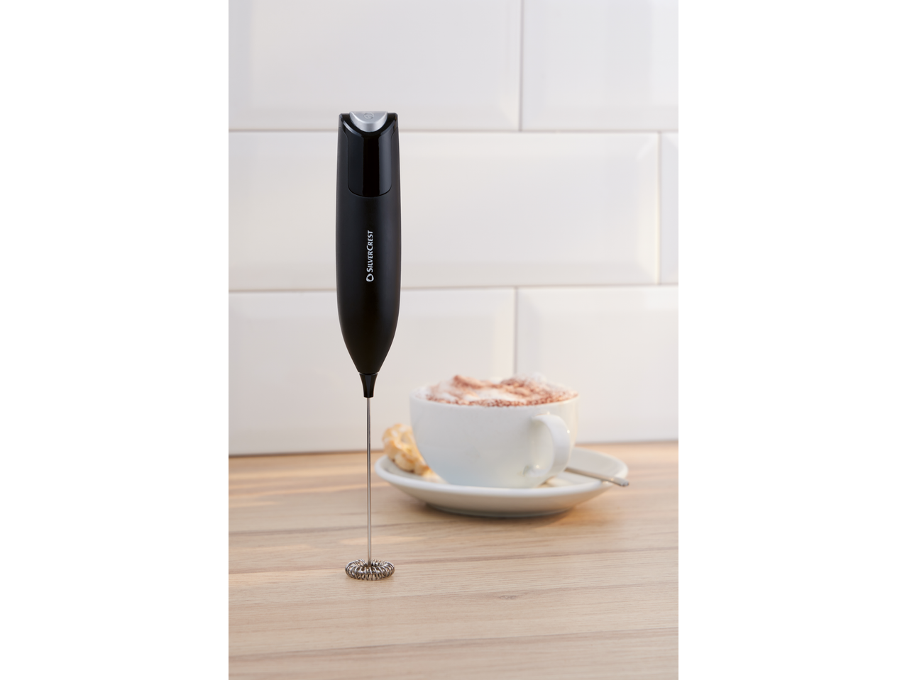 Espumador de leite preto SILVERCREST® com uma chávena de latte ao fundo.