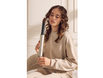 Woman curling her brown hair with a hair styler, wearing a beige sweatshirt.