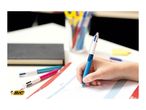 Child's hand writing in a planner with a blue multi-color pen, with other pens and a notebook nearby.