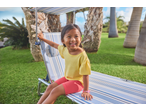 Smiling child on a striped sun lounger in a garden with palm trees.