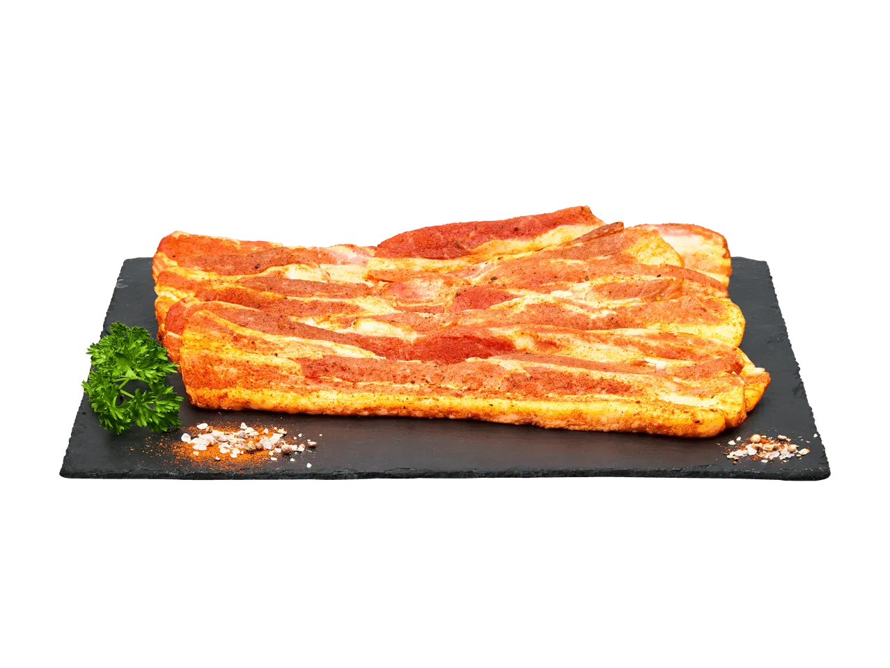 Tranches de poitrine de porc marinées sur une ardoise noire avec persil et épices.