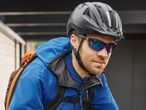 Man in a blue cycling jacket, helmet, and sunglasses with a backpack.