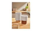 Two storage containers with cereal and cocoa powder on a wooden kitchen counter.