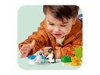 A child playing with toy penguins and a lion cub on a light green surface.