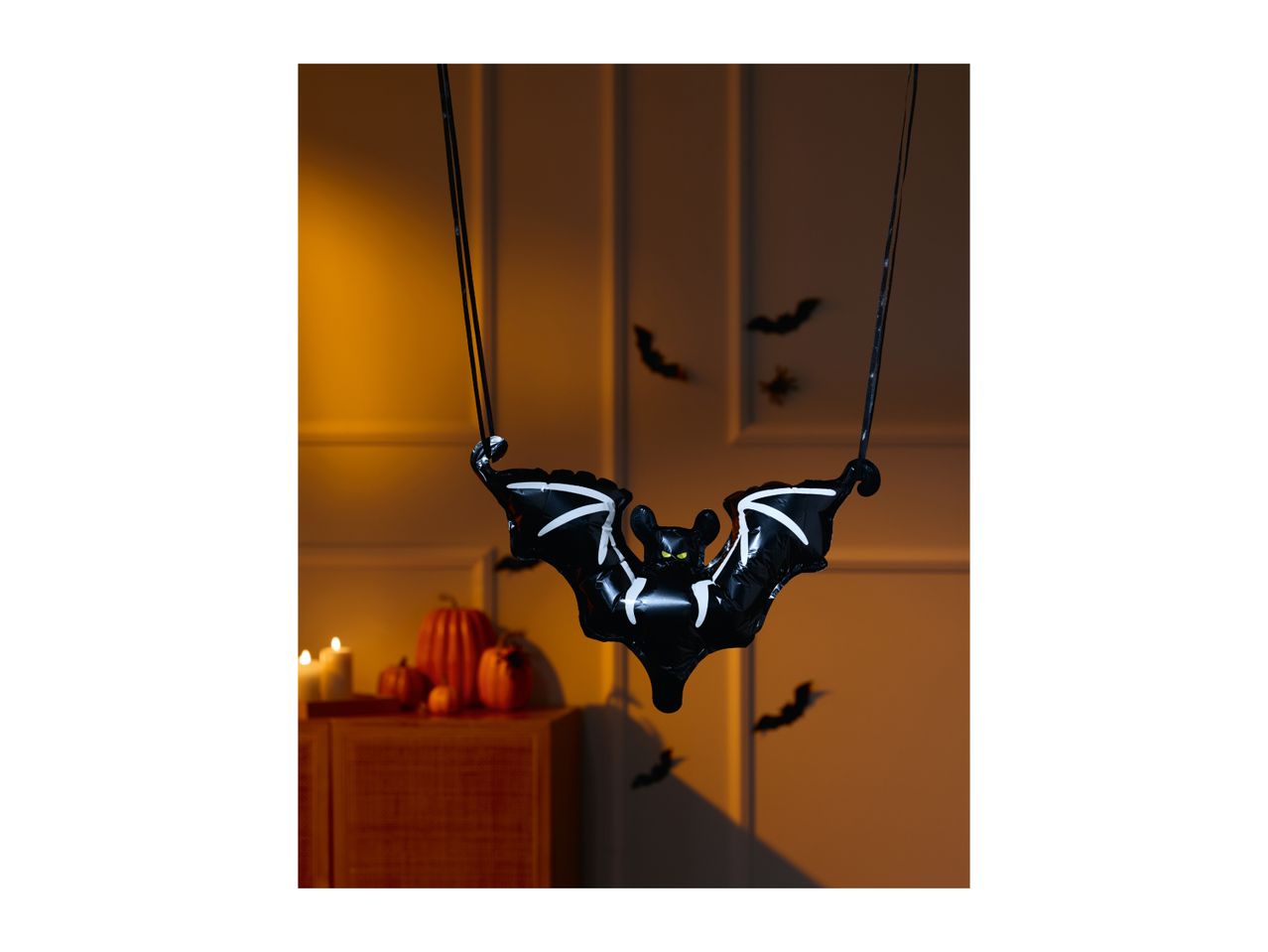 Halloween bat balloon with pumpkins and candles in a dimly lit room.