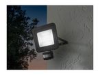 An outdoor LED floodlight with a motion sensor mounted on a textured wall at dusk.