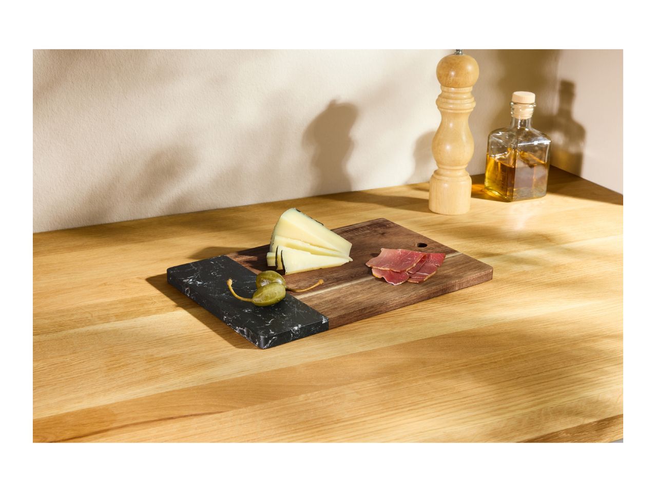 Cheese, capers, and cured meat on a wooden and marble serving board.