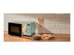 Mint green microwave with an open door, next to a bowl of soup and sliced bread.