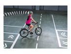 Woman in a pink vest and helmet riding a bicycle on a marked floor with dominoes.