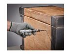Gloved hand using an impact driver to remove a screw from a wooden chest.