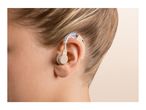 Close-up of a person's ear with a beige hearing aid, showing the device clearly.
