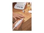 Person using an electric manicure and pedicure set on a wooden table with nail care accessories.