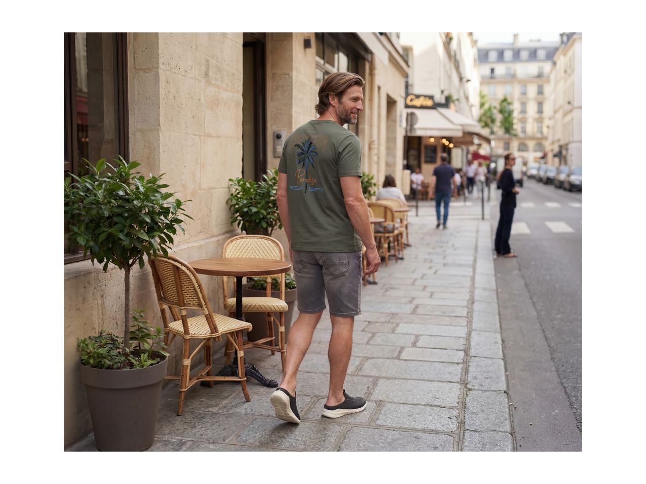 Man in a green t-shirt with a palm tree graphic and grey shorts walking on a city street.