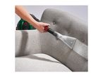 Handheld upholstery cleaner nozzle being used to clean a grey fabric armchair.